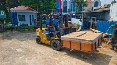 Bogor, Endonezya - 5 Haziran 2025: Sarı CAT forklift işlek endüstriyel depo tesisinde büyük ahşap kargo sandıkları taşıyor