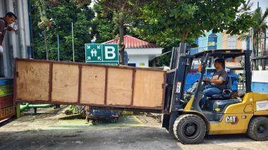 Bogor, Endonezya - 5 Haziran 2025: Sarı CAT forklift operatörü sanayi deposundaki sanayi bölgesindeki tahta kargo kutularını güvenli tahliye işaretleriyle dolduruyor