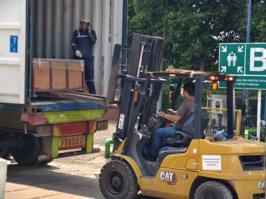 Bogor, Endonezya - 5 Haziran 2025: Sarı forklift nakliye konteynerlerini aktif depo lojistik operasyon merkezindeki nakliye kamyonuna yüklüyor
