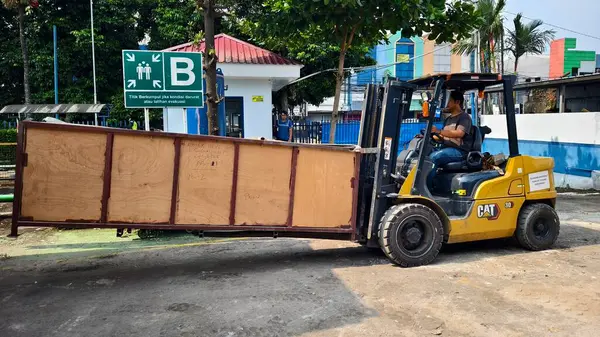 Bogor, Endonezya - 5 Haziran 2025: Sarı CAT forklift operatörü sanayi deposundaki sanayi bölgesindeki tahta kargo kutularını güvenli tahliye işaretleriyle dolduruyor