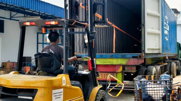 Bogor, Endonezya - 5 Haziran 2025: Sarı forklift nakliye konteynerlerini aktif depo lojistik operasyon merkezindeki nakliye kamyonuna yüklüyor