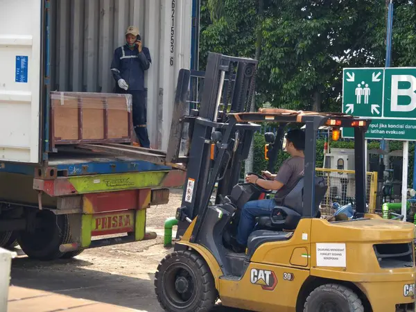 Bogor, Endonezya - 5 Haziran 2025: Sarı forklift nakliye konteynerlerini aktif depo lojistik operasyon merkezindeki nakliye kamyonuna yüklüyor