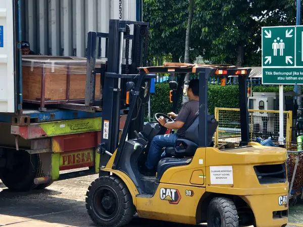 Bogor, Endonezya - 5 Haziran 2025: Sarı CAT forklift operatörü endüstriyel depo tesisinde kargo kamyonuna ahşap sandıklar yüklüyor