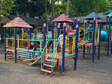 Bogor, Endonezya - 7 Haziran 2025: Ağaçlarla çevrili halka açık bir parkta çocuklar için renkli bir oyun alanı