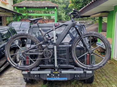 Bogor, Endonezya - 14 Haziran 2025: Premium siyah elektrikli dağ bisikleti (E-bisiklet) elektrikli bir cipin arkasındaki sağlam bir araba rafına güvenli bir şekilde monte edilmiştir.