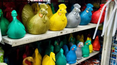 Parlak renkli plastik horoz heykelcikleri bir mağaza ortamında bir rafta sergileniyor..