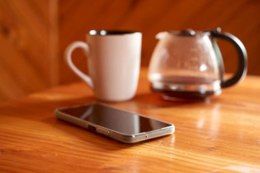 Kahve makinesinde kahve yapmak ahşap bir masada, rahat bir bardak ve akıllı telefon dinlenmesi, rahatlamak ve kahvaltıdan zevk almak için mükemmel bir sabah atmosferi yaratmak.