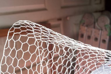 Beyaz kümes teli, arka planda bulanık kutular ve badminton raketleri olan kıvrımlı bir şekil oluşturuyor. Bu da bir depo ya da garaj ortamı olduğunu gösteriyor.