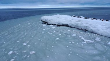 Okyanus akıntıları, buzla dolu sularla buzlu halkalar oluşturur. Karanlık bir kıyı ortamında donmuş bir kayanın ucundan geçer..