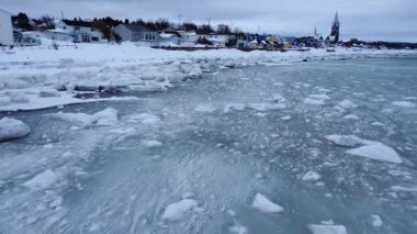 Bir kıyı köyünün kıyı şeridi, karanlık bir kış atmosferinde eriyen kar dalgaları tarafından kıyıya vurulan buz blokları tarafından yutulur..