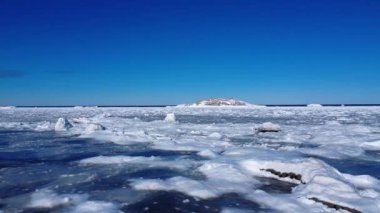 Buz gibi bir okyanusun üzerinden açık mavi gökyüzünün altında yükselen bir kayaya doğru düşük hızda uçarken birkaç küçük deniz kuşu buradan geçer..