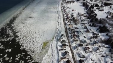 Karla kaplı küçük Gaspesya kıyı köyünün buzlu kıyılarında kış uçuşu. Saint-Ulric-de-Matane, Quebec, Kanada.