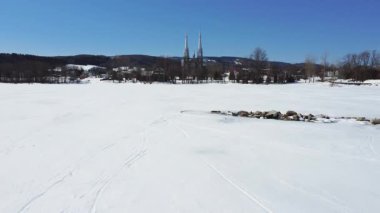 Saint-Pierre-du-Lac Kilisesi 'ne doğru buzla kaplı Matapdia Gölü' nün üzerinden uçuyor bulutsuz mavi gökyüzü altında, Val-Brillant köyü, Kanada, 2025.