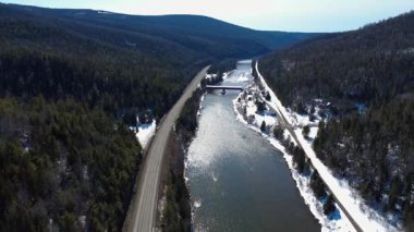 Efsanevi somon balıkçılığı nehri Matapedia Nehri 'ni kaplayan Routhierville Kapalı Köprüsü' nün panoramik manzarası karla kaplı bir dağ vadisinde. Quebec, Kanada, Kış 2025.