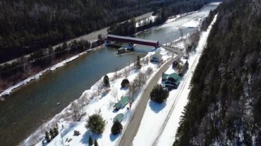 Matapdia Nehri 'nin üzerinde yükselen tarihi Routhierville Kapalı Köprüsü, kışın arka planda karla kaplı bir dağ vadisi. Quebec, Kanada, 2025.