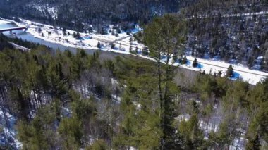 Matapedia Nehri 'nin ve Routhierville Kapalı Köprüsü' nün ağaçların arasından karla kaplı bir dağ vadisine bakan kış manzarası. Quebec, Kanada, 2025.