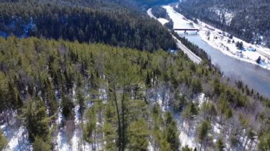 Matapedia Nehri ve Routhierville Kapalı Köprüsü, ağaçların tepesinde, karla kaplı bir dağ vadisinde kış manzarası. Quebec, Kanada, 2025.