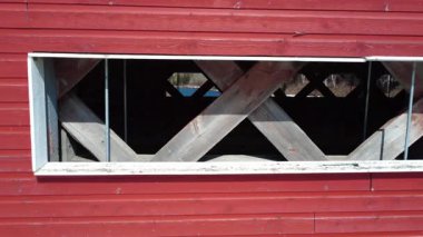 Üstü kapalı bir köprünün, dış duvarları kırmızı olan geniş yan pencerelerinin kenardan kenarına bakışı, x şeklindeki ahşap yapıları ortaya çıkarıyor..