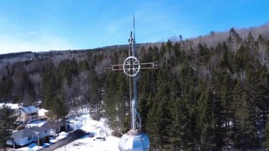 Bir kilisenin üzerindeki haç etrafında dönerek, bir köprü ve demiryolu ile çevreleyen köyün kırsal manzarasını ortaya çıkarıyor. Sainte-Florence, Quebec, Kanada, 2025.