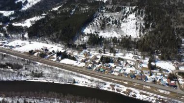 Karla kaplı bir dağın dibindeki kırsal bir arazinin havadan görünüşü. Evleri ve köy yoluna paralel giden bir tren yolu var. Sainte-Florence, Quebec, Kanada, 2025.