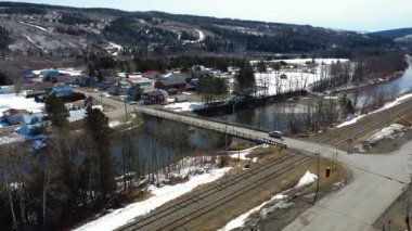 Demiryolu ile çevrili Matapedia Nehri 'ni geçen bir araç, küçük bir kırsal köyde kar parçalarıyla benekli bir köprüden geçer. Sainte-Florence, Quebec, Kanada, 2025.