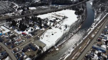 Göz alabildiğine dolambaçlı bir nehrin geçtiği dağ vadisindeki karla kaplı bir köyün panoramik hava görüntüsü. Matapedia Nehri, Sainte-Florence, Quebec, Kanada, 2025.