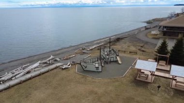 Büyük bir tuzlu su koyunun kenarında sarı çimenli, eski bir tekne gibi dizayn edilmiş boş bir çocuk parkının havadan görünüşü. Maria, Quebec, Kanada, 2025.