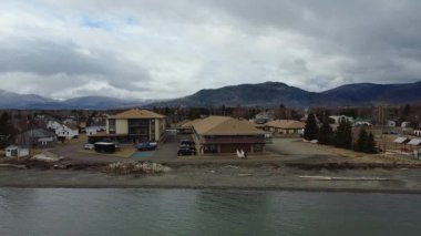 Arka planda bulutlu bir gökyüzünün altında dağ sırası bulunan sakin bir körfezin kıyısındaki büyük bir konuttan çekilen hava görüntüleri. Maria, Quebec, Kanada, 2025.