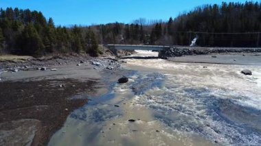 Tartigou Nehri 'nin ağzına kadar uzanan bir köprü, kahverengi kaynak sularını St. Lawrence nehrinin kıyılarına püskürtür..