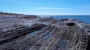 Kayalık jeolojik oluşumların hava görüntüsü mavi bir gökyüzünün altında alçak gelgitle açığa çıkan kıyı şeridini oluşturuyor. Baie-des-Sables, Quebec, Kanada, 2025.