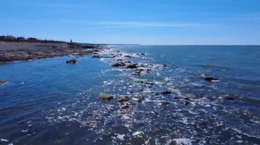 St. Lawrence Nehri kıyısı boyunca insansız hava aracı uçuşu. Güneşin yansımalarının dalgalar ve kayalar arasında patladığı yer. Gözün görebildiği kadar mavi bir okyanus. Baie-des-Sables, Quebec, Kanada, 2025.