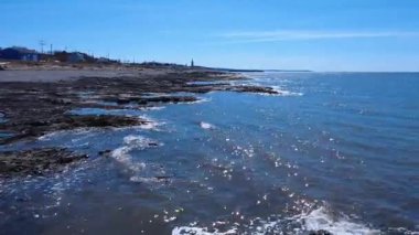 St. Lawrence 'ın kıyılarında uçarken, güneşin yansımalarının mavi bir okyanus ve ufukta bir kilise kulesi ile dalgalar arasında parladığı yerde. Baie-des-Sables, Quebec, Kanada, 2025.