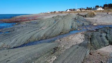 St. Lawrence Nehri, Baie-des-Sables, Quebec, Kanada, 2025 boyunca bulutsuz mavi bir gökyüzü altında tortulu kayaların jeolojik oluşumu bir plajda yüzeye çıkar..
