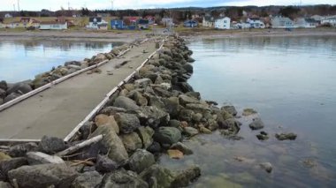 Bir sahil köyü ve terk edilmiş eski rıhtımı, deniz kerestelerinin yığıldığı sakin sahilde yıkanıyor. Baie-des-Sables, Quebec, Kanada, 2025.