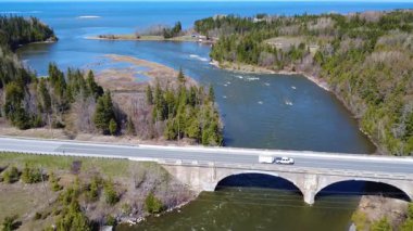 Mitis Nehri 'nin ağzının St. Lawrence Nehri' ne olan panoramik hava görüntüsü ve çift kemerli yol köprüsünü bir kamyon ve römorku geçti. Quebec, Kanada, 2025.