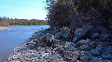 Güneşli bir günde, kayalık bir burnun yanındaki nehirde kürek çeken iki raket. Mitis Nehri, Quebec, Kanada, 2025.