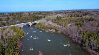 Güçlendirilmiş betondan yapılmış çift kemerli bir yol köprüsünün havadan görünüşü, birkaç araba tarafından geçildi, bir bahar ormanının içinden akan bir somon nehrine yayıldı. Arthur-Bergeron Köprüsü, Quebec, Kanada, 2025.