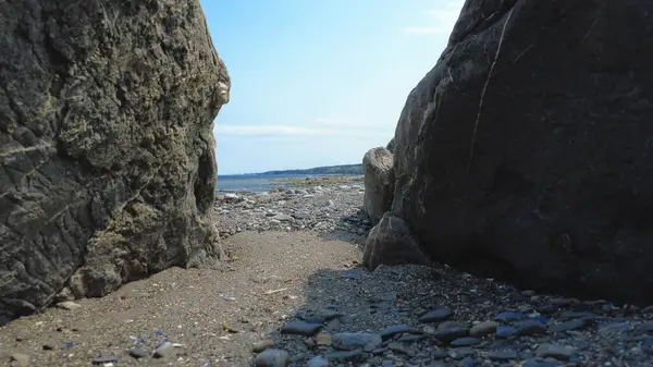 Coastal landscape featuring large rock formations framing a sea view under a blue sky, depicting a tranquil and rugged natural setting.