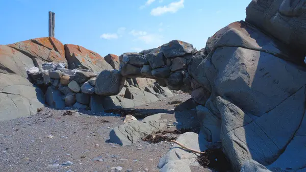 Mavi bir gökyüzünün altında kumlu bir plajın kıyısında iki jeolojik oluşumu birbirine bağlayan eski kayaların bir araya gelmesinden oluşan bir kemer..