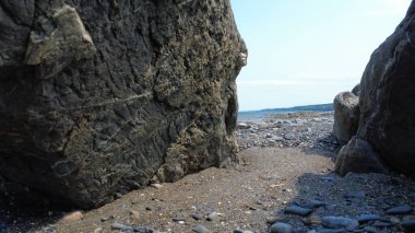 Dalgaların çekildiği kayalık bir sahil manzarası sahilin iki kaya duvarı arasındaki geçitte beliriyor..