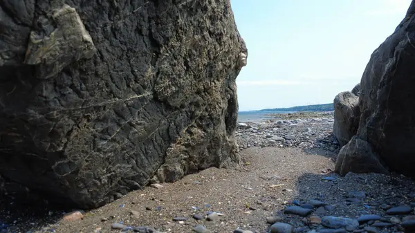 Dalgaların çekildiği kayalık bir sahil manzarası sahilin iki kaya duvarı arasındaki geçitte beliriyor..