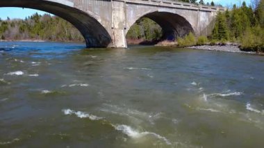 2025 'te Quebec, Kanada' daki sel baskınıyla kahverengileşen Mitis Nehri 'nin üzerindeki beton kemerin altından alçak geçiş yapan bir dron tarafından çekilen video..