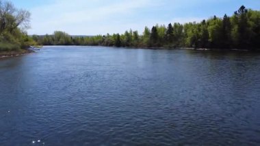 Işıldayan suları ile rahatlatıcı bir nehir yemyeşil manzaralar ve açık mavi gökyüzünün altında bir kilise kulesi olan pitoresk kırsal bölgede esiyor. Mitis Nehri, Fiyat, Quebec, Kanada.