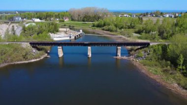 Bir demiryolu köprüsü altındaki insansız hava aracı uçuşu hidroelektrik barajının rezervuarına uzanan üç güçlendirilmiş beton sütun tarafından destekleniyor. Mitis-1 Elektrik Santrali, Price, Quebec, Kanada. 2025.