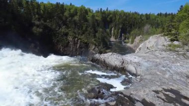 Bir orman şelalesinin tepesine yaklaşıyoruz. Kayalık kayalıklar arasındaki büyük bir çukura düşüyor ve bir gökkuşağı yaratıyor. Mitis Nehri, Fiyat, Quebec, Kanada.