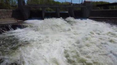 Bir dron videosu çağlayan bir nehrin üzerinden uçarak bir hidroelektrik barajının sızıntı yolundan geçer ve su deposunun üzerindeki bir geçide ulaşır. Mitis-1 Üretim İstasyonu, Fiyat, Quebec, Kanada.