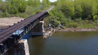Beton sütunlar arasında sakin bir nehir akıyor, yüzen ölü odunlar birikiyor, eski bir demiryolu köprüsünün altında, yemyeşil bitki ve kayalarla çevrili..