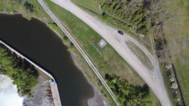 Küçük bir helikopter iniş pistinin, siyah bir arabanın ve büyük bir şelalenin tepesindeki hidroelektrik barajına güç veren rezervuarın yakınındaki evlerin havada dönen görüntüsü. Mitis-1 elektrik santrali, Price, Quebec, Kanada.