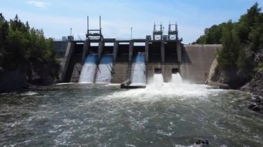 Çağlayarak akan, yüksek akışlı su boşaltımlı beton bir hidroelektrik baraj yapısı ormandaki bir kale gibi bir nehirde duruyor. Mitis-2 Üretim İstasyonu, Price, Quebec, Kanada.