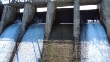 Hidroelektrik bir barajın taşma kapılarının yakın çekim görüntüsü, su akıntısını serbest bırakarak yapının üzerinde yükselen şelaleler yaratarak rezervuarının panoramik bir görüntüsünü sağlıyor. Mitis-2 Barajı, Mitis Nehri, Quebec, Kanada.